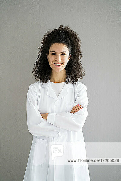 Smiling female doctor with arms crossed against wall at clinic