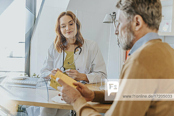 Männlicher Patient  der mit dem Arzt über den Impfpass diskutiert  während er im Büro bei COVID-19 sitzt