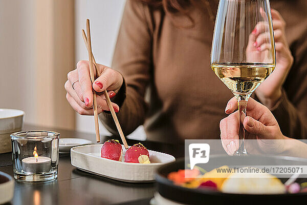 Young women eating sushi while drinking wine at restaurant