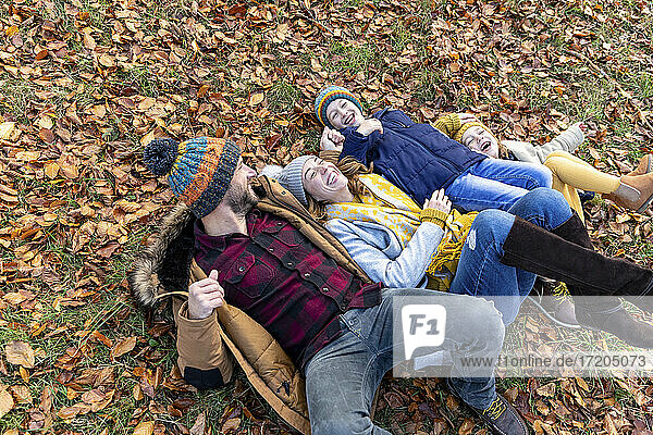 Glückliche Familie  die auf Blättern im Wald liegend spielt