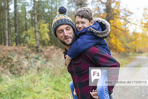 Smiling boy enjoying while piggybacking on father in forest