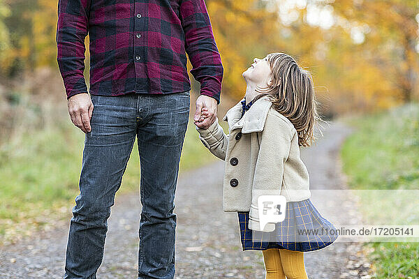 Smiling daughter holding hand of father while standing at forest path
