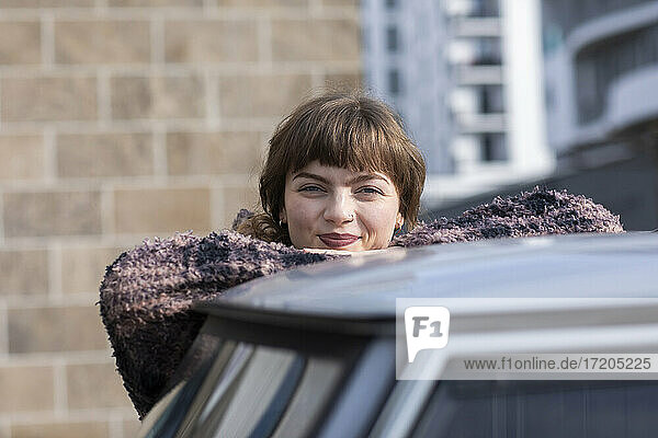 Junge Frau lächelt  während sie sich auf dem Autodach abstützt