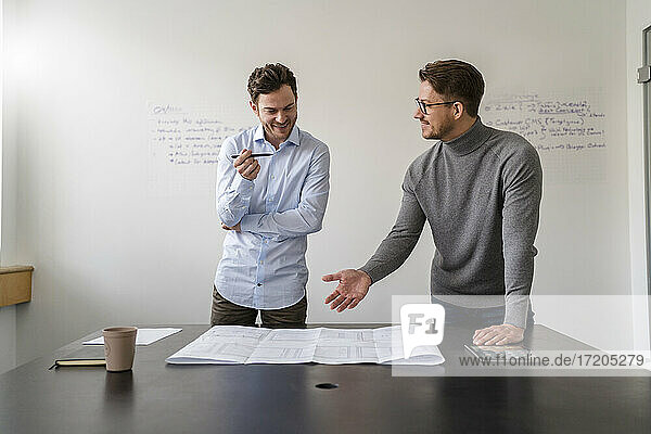 Geschäftsleute  die während eines Treffens im Büro an der Wand über einen Bauplan diskutieren