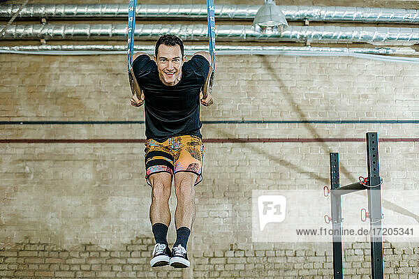 Smiling man hanging on gymnastic rings at health club