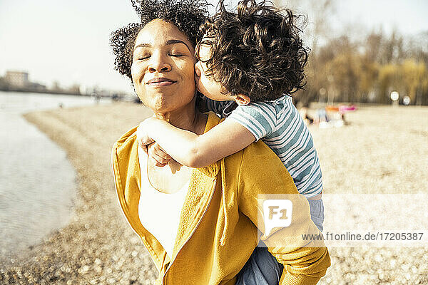 Boy kissing while piggybacked by mother on sunny day