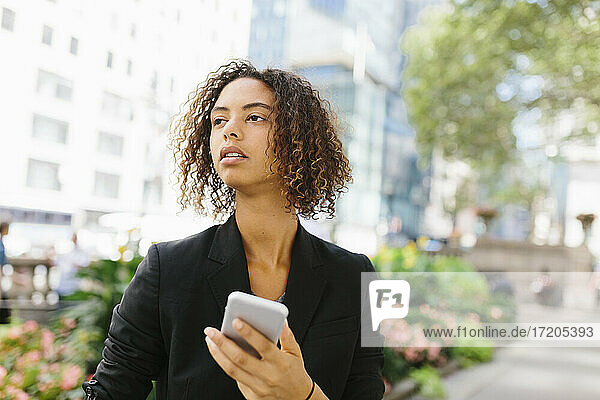 Thoughtful Afro female entrepreneur with smart phone in city