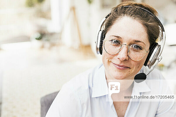 Lächelnde weibliche Fachkraft mit Brille und drahtlosen Kopfhörern
