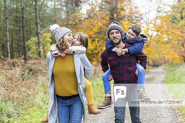 Parents piggybacking children while walking in forest during autumn