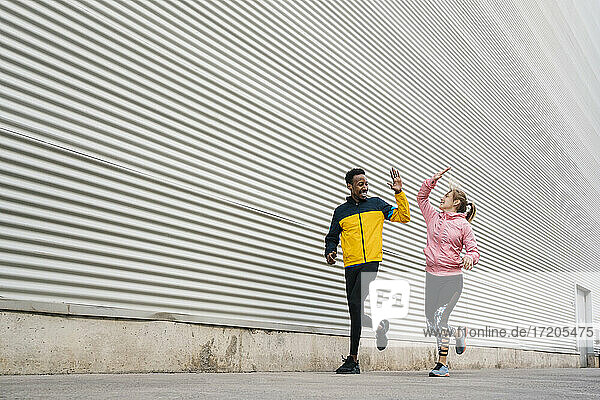 Male and female sportsperson doing high-five while exercising by wall