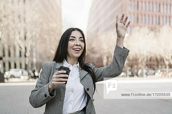 Reife Geschäftsfrau mit Kaffeetasse  die in der Stadt einem Taxi zuwinkt
