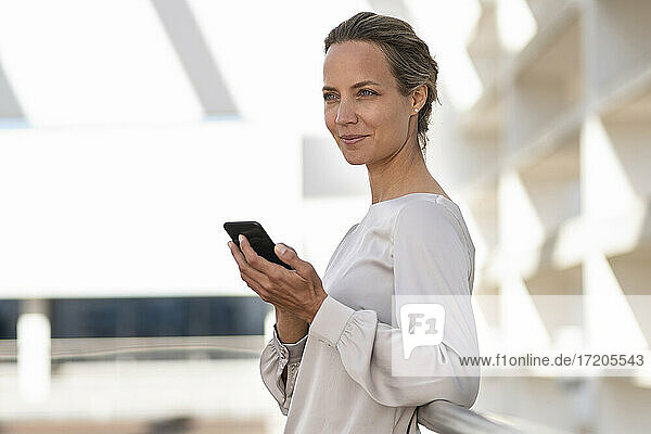 Geschäftsfrau  die ein Smartphone benutzt  während sie auf einer Büroterrasse steht