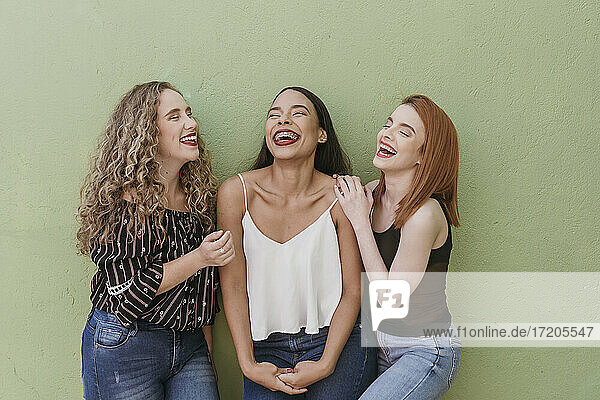 Multiethnische Freundinnen lachend vor grüner Wand