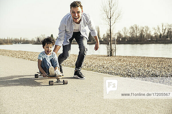 Cheerful man and boy playing with skateboard on road during sunny day