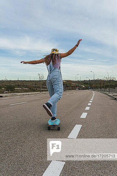 Woman in bib overall skating with skateboard on road
