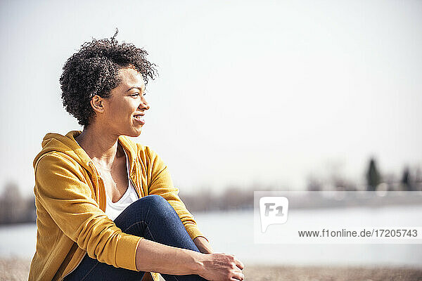 Lächelnde Frau sitzt im Freien an einem sonnigen Tag