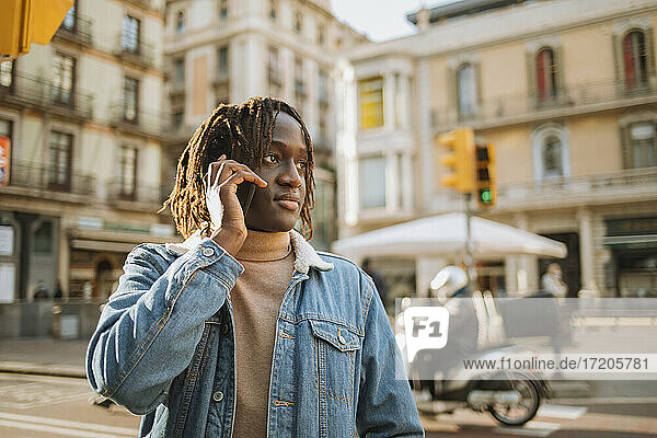 Young man with locs hairstyle talking on phone while looking away in city
