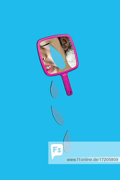 Reflection of girl on hand mirror with teardrops over blue background