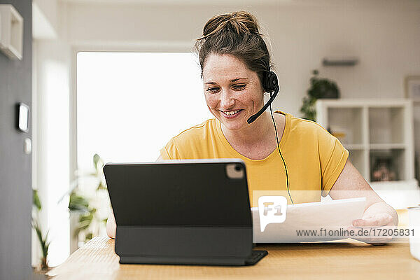 Lächelnde Geschäftsfrau mit Kopfhörern bei einer Videokonferenz zu Hause