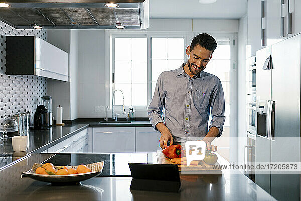 Smiling man with vegetables standing at kitchen counter