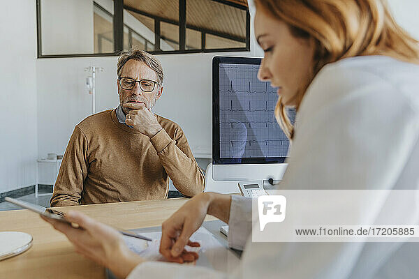Arzt bespricht sich mit einem Patienten über ein digitales Tablet  während er in der Klinik sitzt
