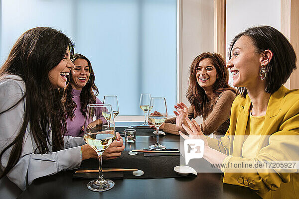 Female friends with wine glasses laughing while sitting at table in restaurant