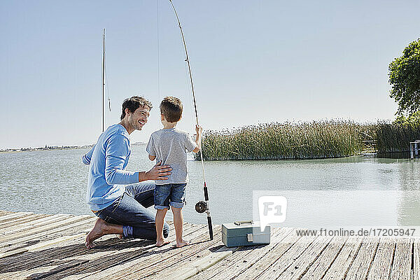 Father smiling at son standing with fishing rod on pier