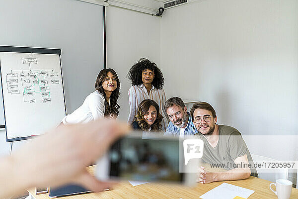 Mann fotografiert männliche und weibliche Unternehmer mit dem Smartphone im Sitzungssaal eines Büros
