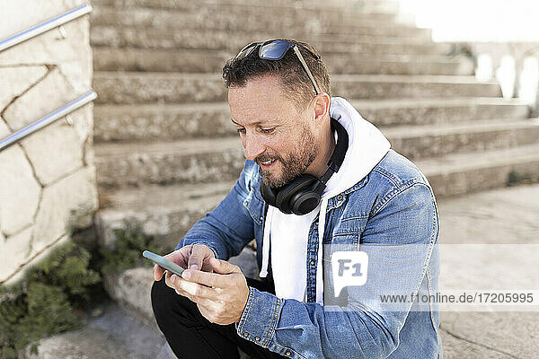 Mann mit Kopfhörern  der sein Smartphone benutzt  während er auf einer Treppe sitzt
