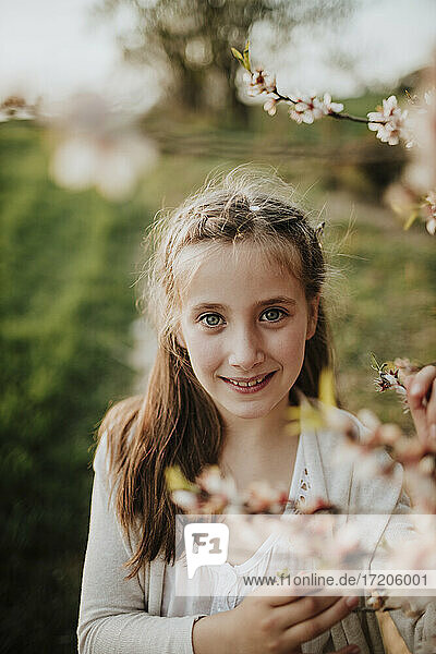 Nettes Mädchen lächelt  während es neben Mandelbaumblüten steht