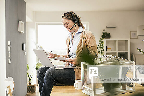 Female professional examining document while sitting with laptop at home