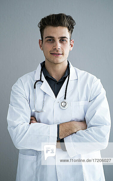 Male handsome doctor with arms crossed against gray wall