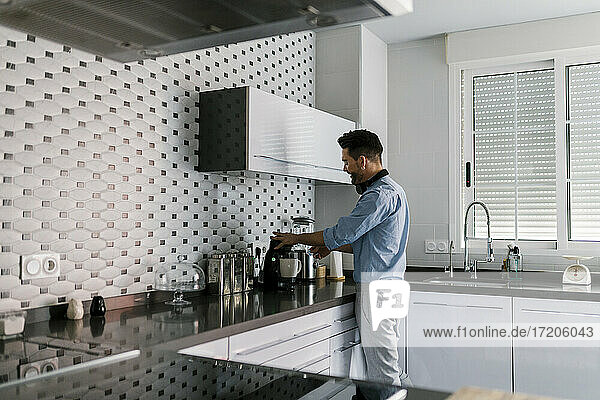 Mann mit Kopfhörern  der eine Kaffeemaschine benutzt  während er in der Küche zu Hause steht