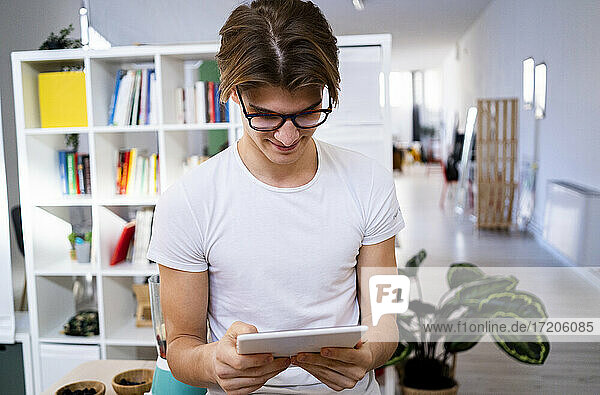 Junger Mann surft im Internet über ein digitales Tablet in der Küche zu Hause