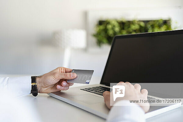 Geschäftsmann  der eine Kreditkarte hält  während er einen Laptop im Büro benutzt