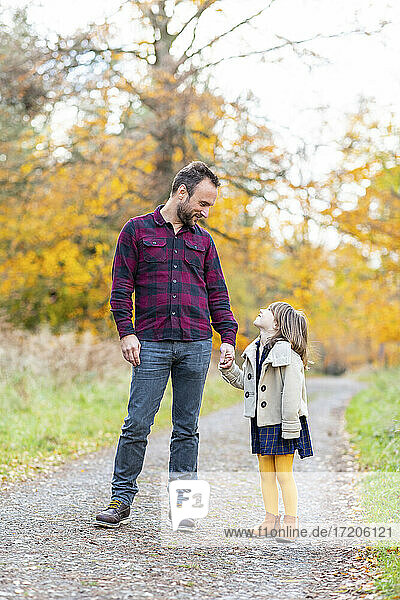 Lächelnder Vater  der seine Tochter anschaut  während er im Wald steht und die Hände hält