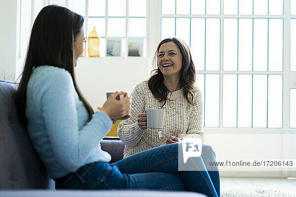 Glückliche Mutter und Tochter mit Kaffeetasse auf dem Sofa zu Hause sitzend