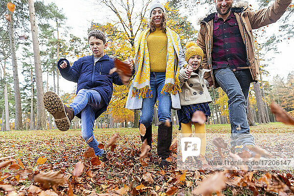 Lächelnde Familie spielt mit gefallenen Blättern beim Spaziergang im Wald