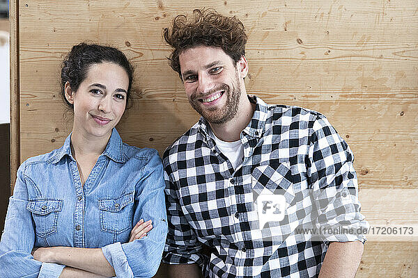 Lächelnde männliche und weibliche Unternehmer an einer Holzwand