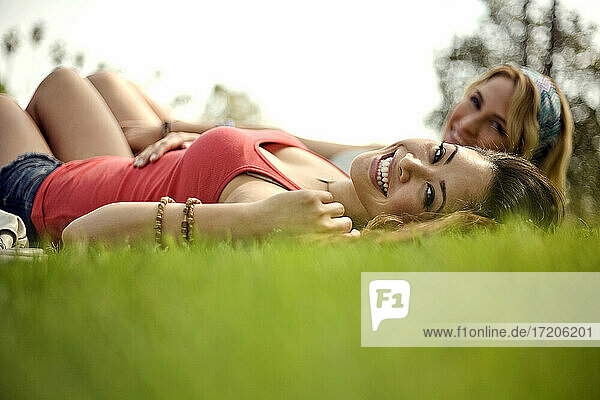 Schöne fröhliche Frau mit Freundin im Gras liegend im Park