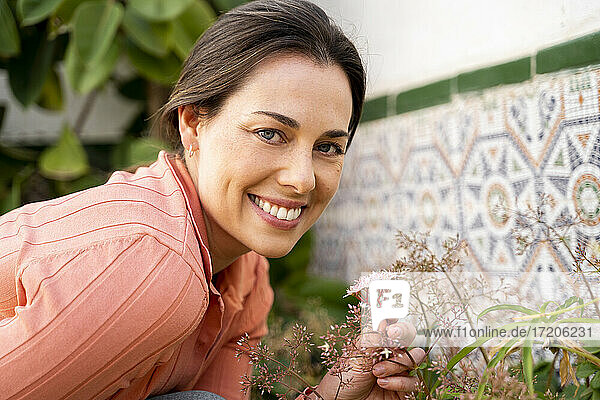 Schöne lächelnde Frau mit blauen Augen hält Blumen im Garten