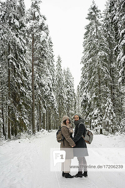 Paar mit Rucksack hält sich an den Händen  während es im Winter im Wald steht