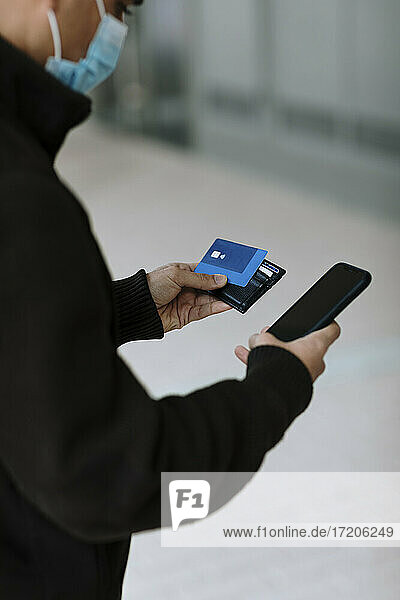 Junger Mann mit Kreditkarte und Smartphone bei einer Online-Zahlung während der COVID-19