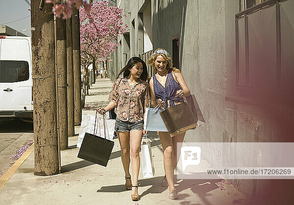 Fröhliche Frauen  die Einkaufstaschen tragen  während sie auf dem Bürgersteig in der Stadt spazieren gehen