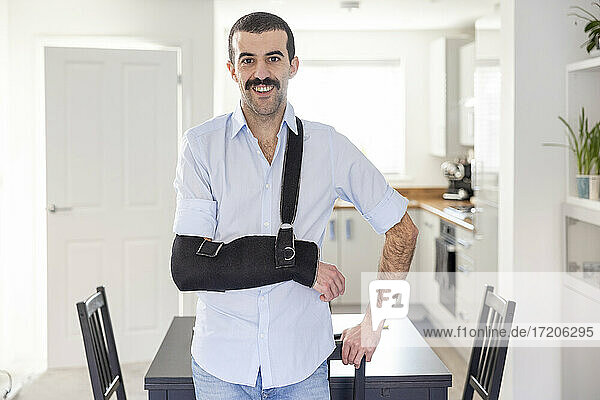 Smiling man wearing arm sling standing by table at home