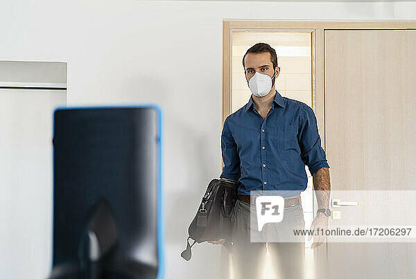 Geschäftsmann mit Gesichtsschutzmaske  der einen Assistenzroboter betrachtet  während er im Büro steht