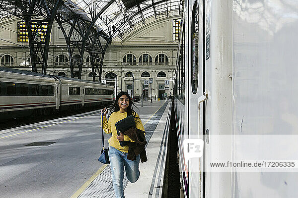 Lächelnde Frau mit Laptoptasche läuft auf dem Bahnsteig  um den Zug zu erreichen
