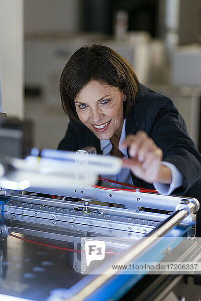 Smiling businesswoman examining machinery at illuminated factory