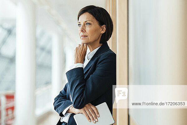 Thoughtful businesswoman with hand on chin against wall in office
