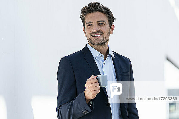 Geschäftsmann trinkt Kaffee und steht vor einer weißen Wand